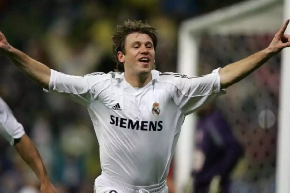 Jugador de fútbol celebrando un gol con los brazos extendidos mientras viste el uniforme blanco del Real Madrid.