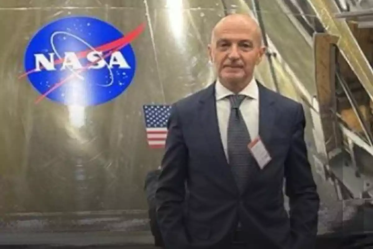 Un hombre de traje y corbata está de pie frente a un logotipo de la NASA y una bandera de Estados Unidos.