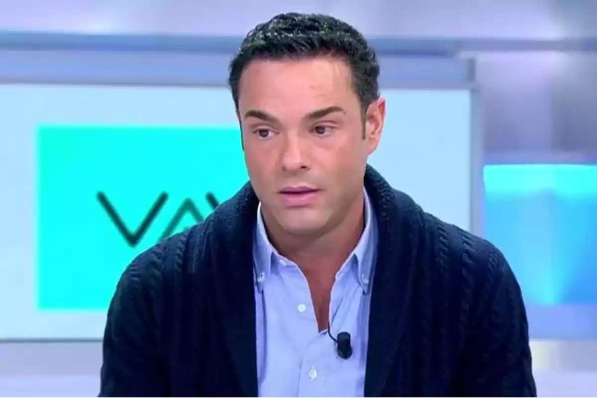 Hombre con cabello oscuro y suéter azul hablando en un programa de televisión. Hombre con cabello oscuro y suéter azul hablando en un programa de televisión.