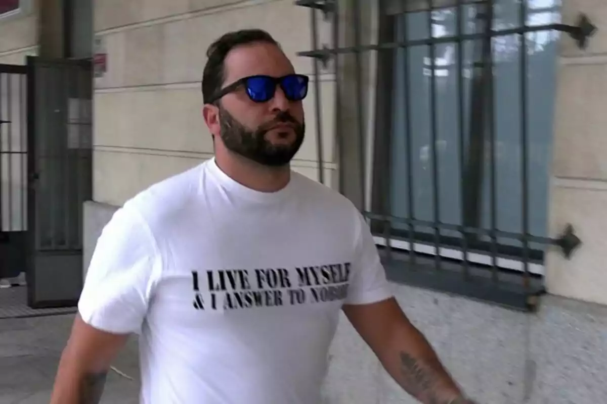 Antonio Tejado con barba y gafas de sol camina por la calle vistiendo una camiseta blanca con un mensaje en inglés.