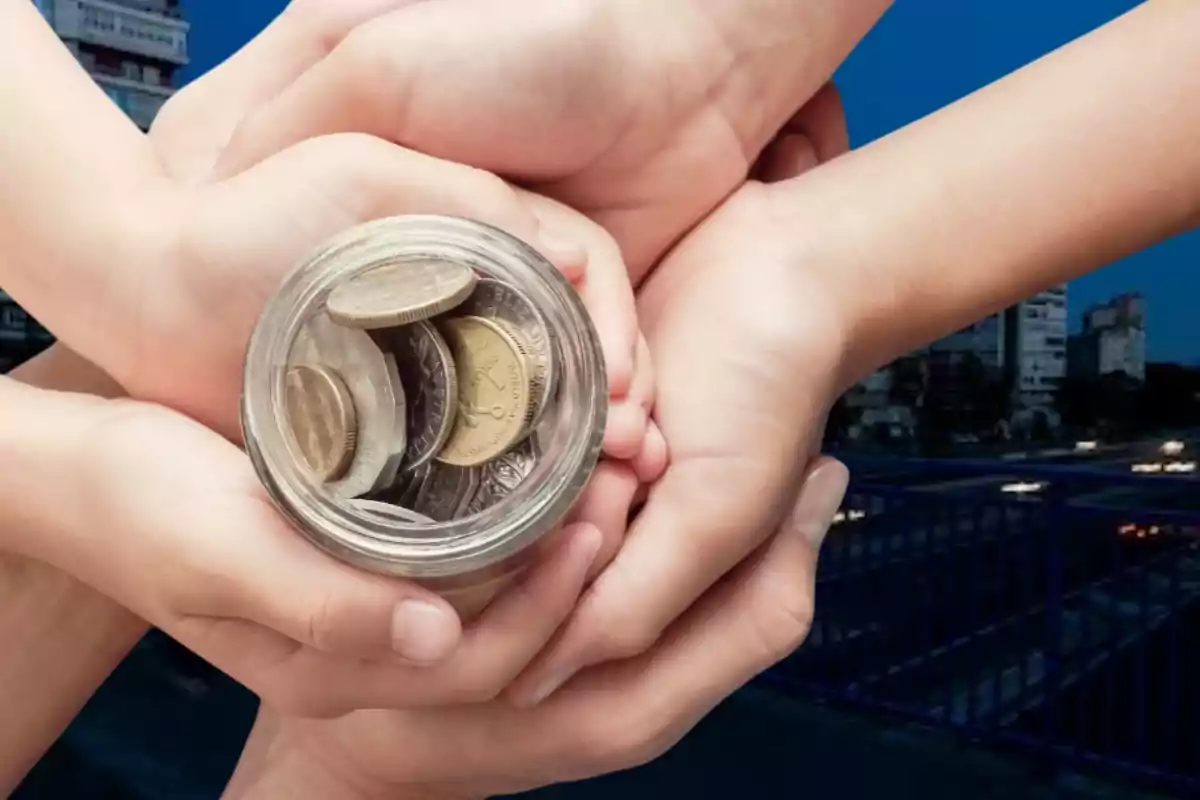 Manos sosteniendo un frasco lleno de monedas con un fondo urbano.