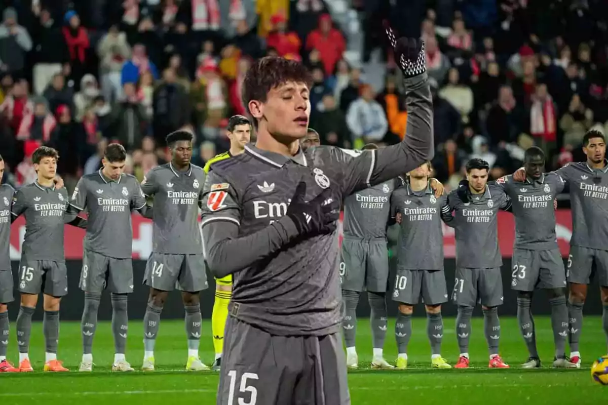 Un jugador de fútbol del Real Madrid con el uniforme gris levanta el brazo mientras sus compañeros están alineados en el fondo.