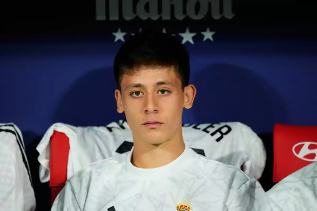 Un joven con camiseta blanca sentado en un banquillo deportivo.