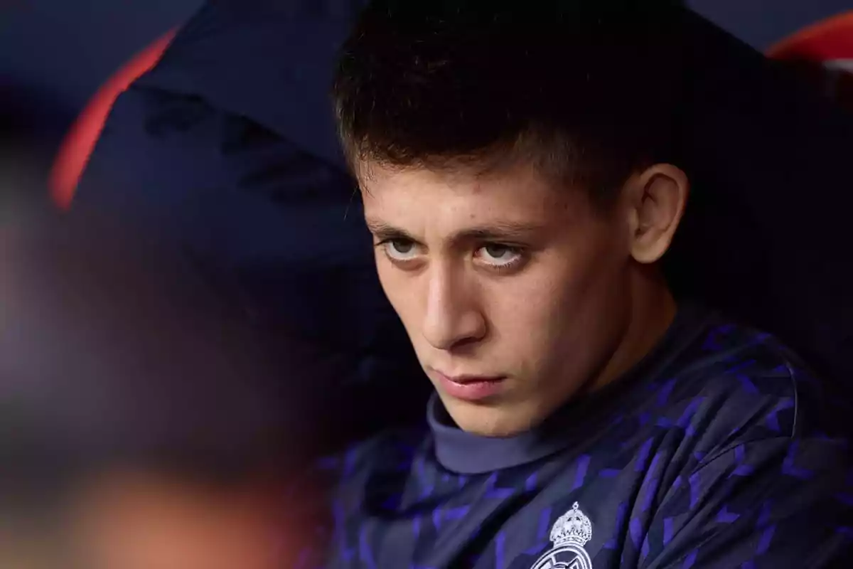 Un joven con expresión seria y concentrada, vistiendo una camiseta deportiva azul con un escudo en el pecho.