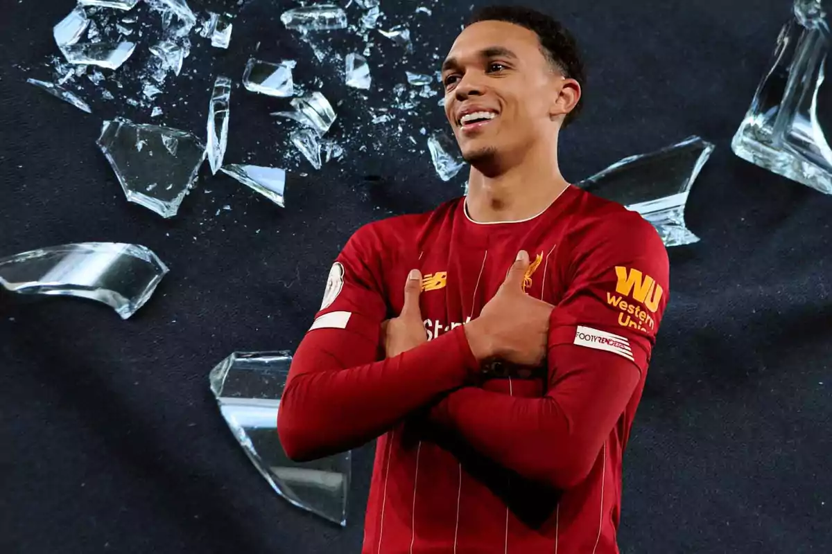 Jugador de fútbol con uniforme rojo posando frente a un fondo de vidrios rotos.