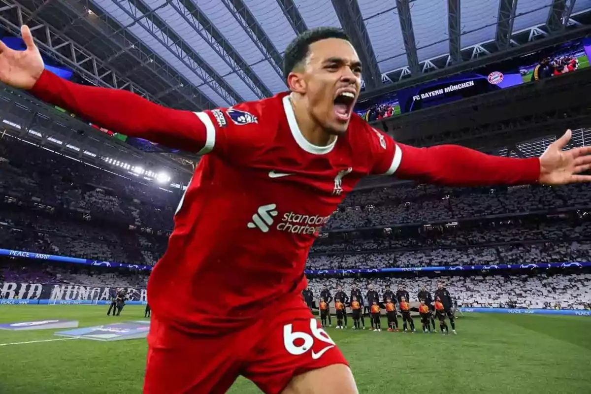 Un jugador de fútbol con uniforme rojo celebra con los brazos extendidos en un estadio lleno de espectadores.