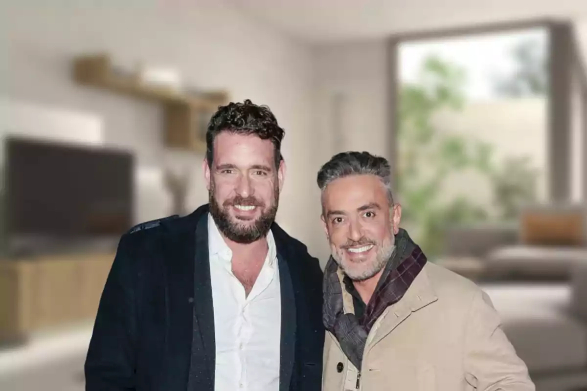 Dos hombres sonrientes posan juntos en una sala de estar moderna y bien iluminada.