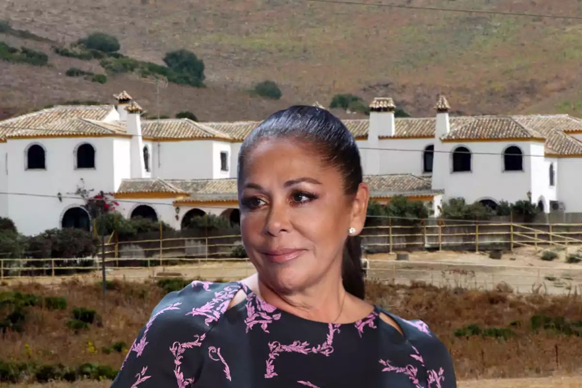 Una mujer con el cabello recogido y una blusa con estampado floral se encuentra frente a una casa de estilo tradicional en un entorno rural.