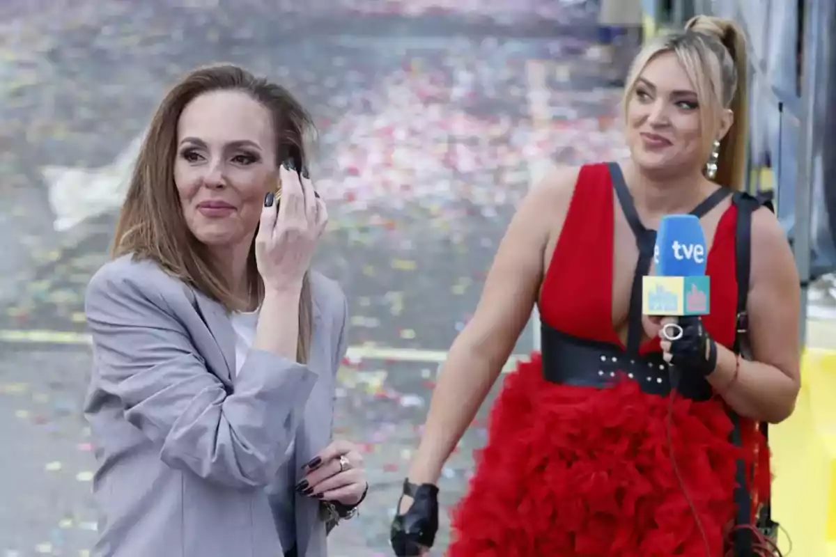 Dos mujeres en un evento al aire libre, una de ellas sostiene un micrófono de televisión. Dos mujeres en un evento al aire libre, una de ellas sostiene un micrófono de televisión.