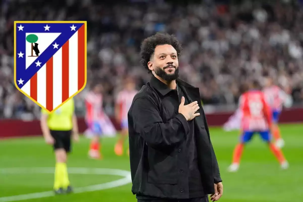 Un hombre con la mano en el pecho en un estadio de fútbol con el escudo del Atlético de Madrid en el fondo.