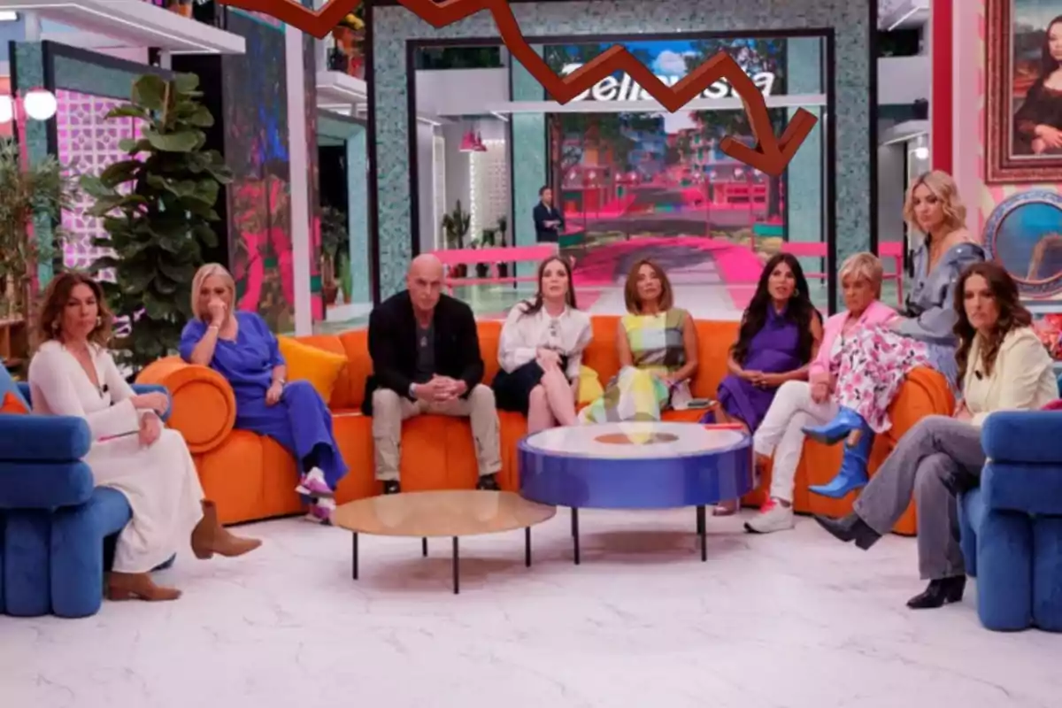 Un grupo de personas está sentado en un set de televisión colorido, con sofás naranjas y azules, mientras una flecha descendente aparece en la parte superior de la imagen.