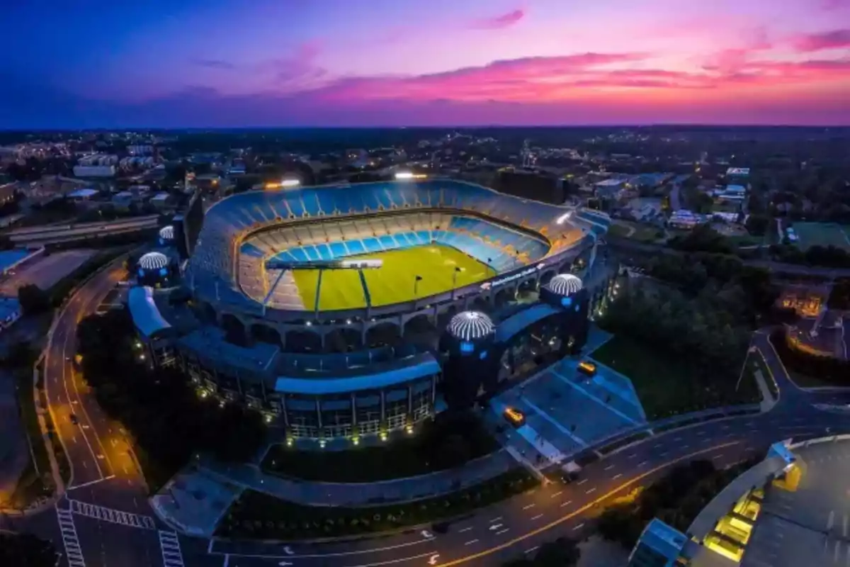 Vista aérea de un estadio iluminado al atardecer con gradas vacías y cielo colorido Vista aérea de un estadio iluminado al atardecer con gradas vacías y cielo colorido