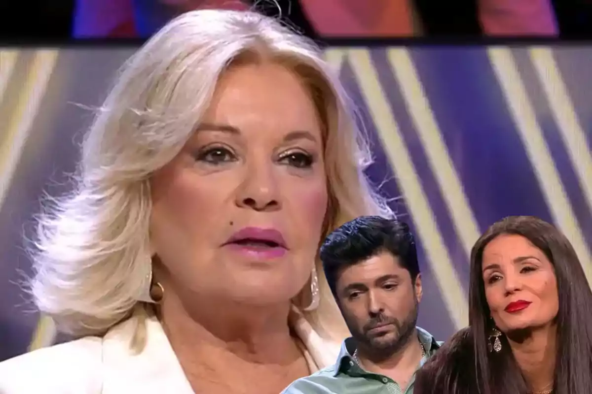 Una mujer rubia en primer plano con expresión seria y dos personas más pequeñas en la esquina inferior derecha, un hombre con barba y una mujer de cabello oscuro, todos en un entorno de estudio de televisión.