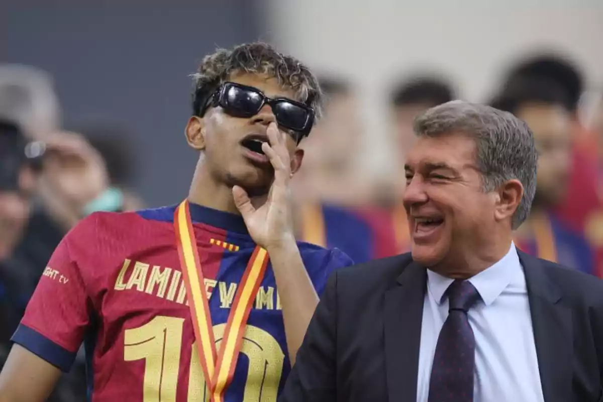 Un joven con gafas de sol y medalla celebra junto a un hombre mayor que sonríe ambos en un ambiente deportivo.