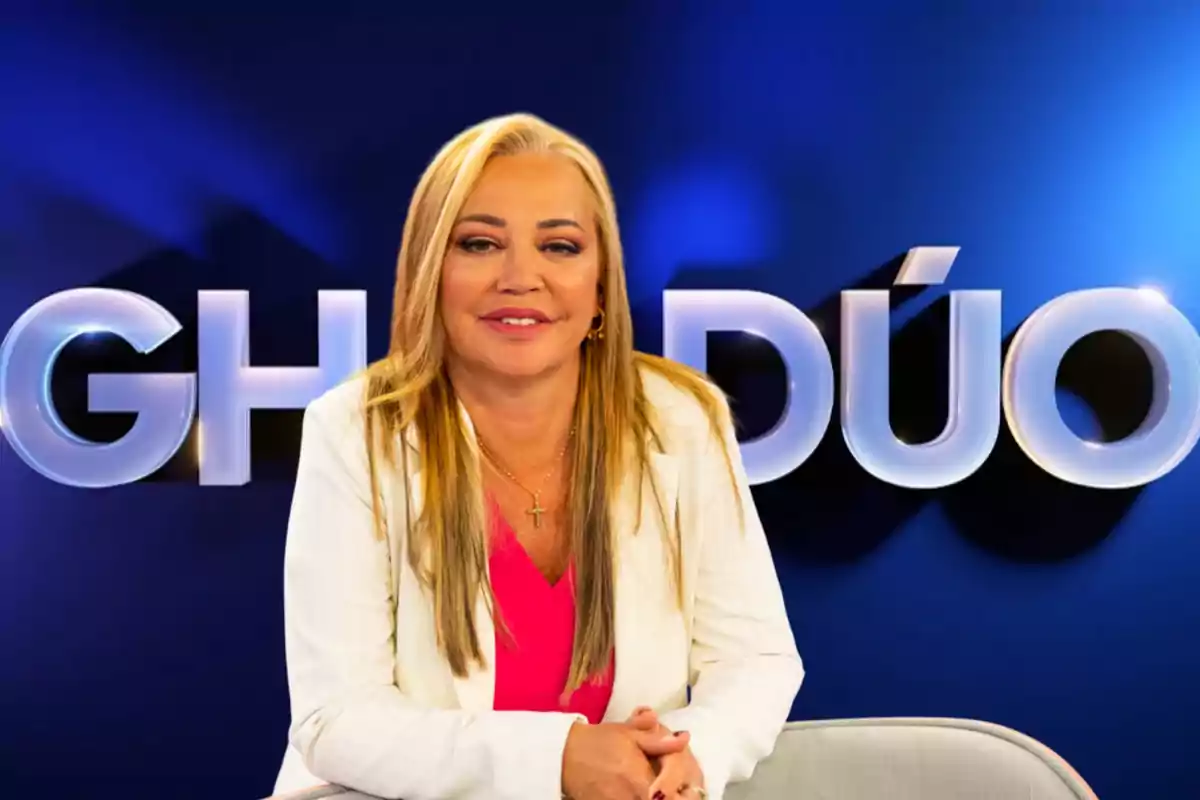 Mujer rubia con chaqueta blanca y blusa rosa frente al logo de GH DÚO en un fondo azul.