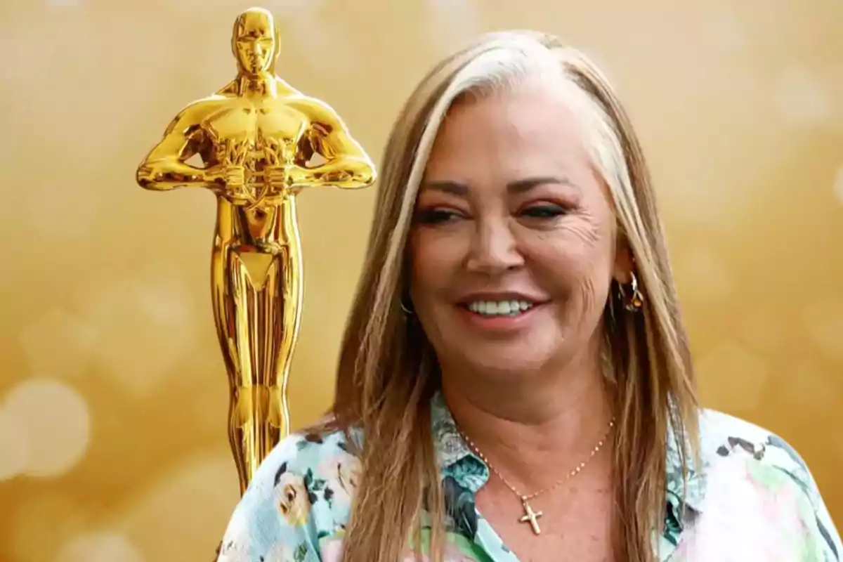 Una mujer sonriente con cabello rubio y una camisa floral está al lado de una estatuilla dorada de un premio Oscar sobre un fondo dorado.