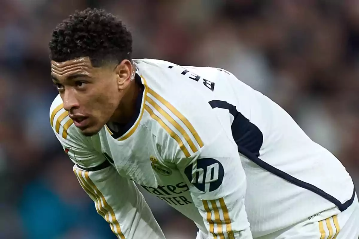 Jugador de fútbol con uniforme blanco y detalles dorados, inclinado hacia adelante en un campo de juego.