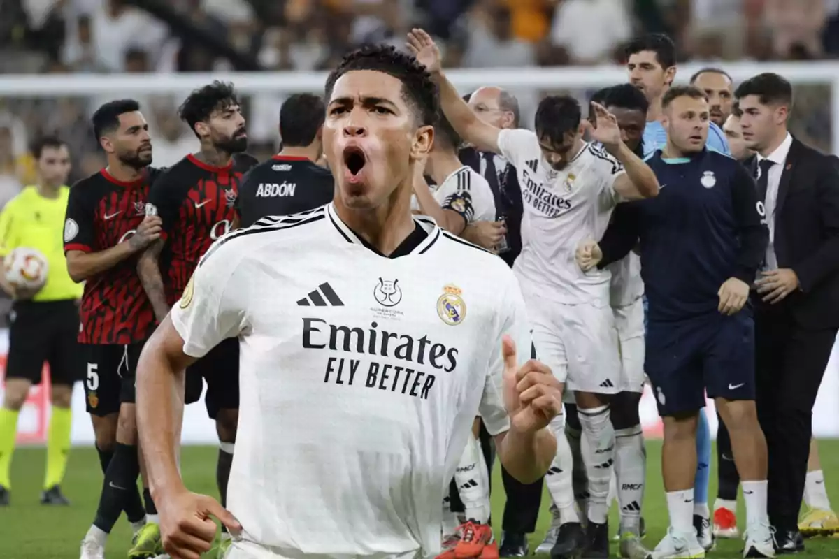 Jugador de fútbol celebrando en el campo con compañeros y rivales al fondo.