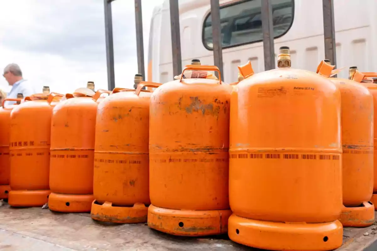 Varias bombonas de gas butano de color naranja en fila junto a un vehículo.