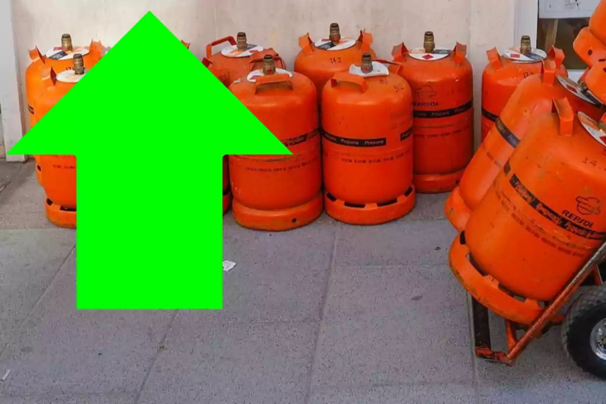 Un grupo de cilindros de gas naranja junto a una pared con una flecha verde grande apuntando hacia arriba.