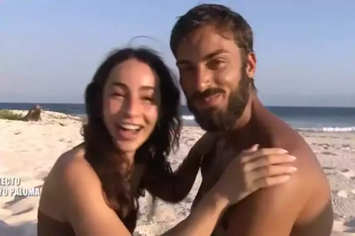 Una pareja sonriente se abraza en la playa con el mar de fondo. Una pareja sonriente se abraza en la playa con el mar de fondo.