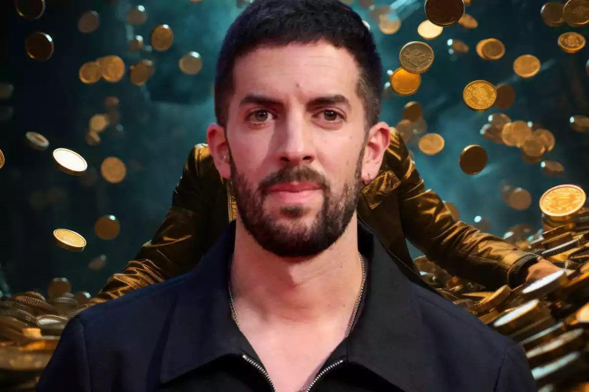 Un hombre con barba y cabello corto, vestido con una chaqueta oscura, está frente a un fondo lleno de monedas doradas flotando en el aire.