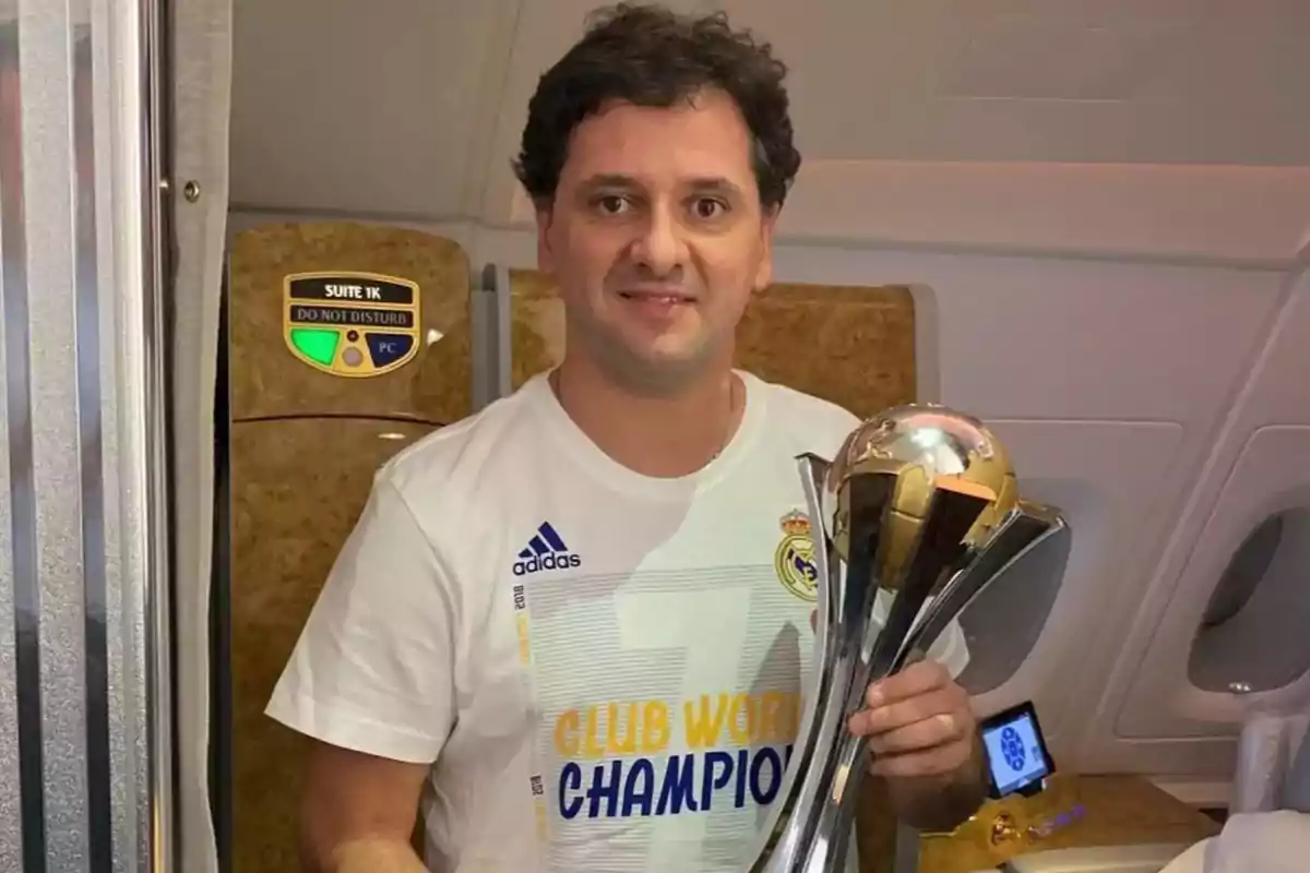 Hombre con camiseta de Real Madrid sosteniendo un trofeo dentro de un avión.