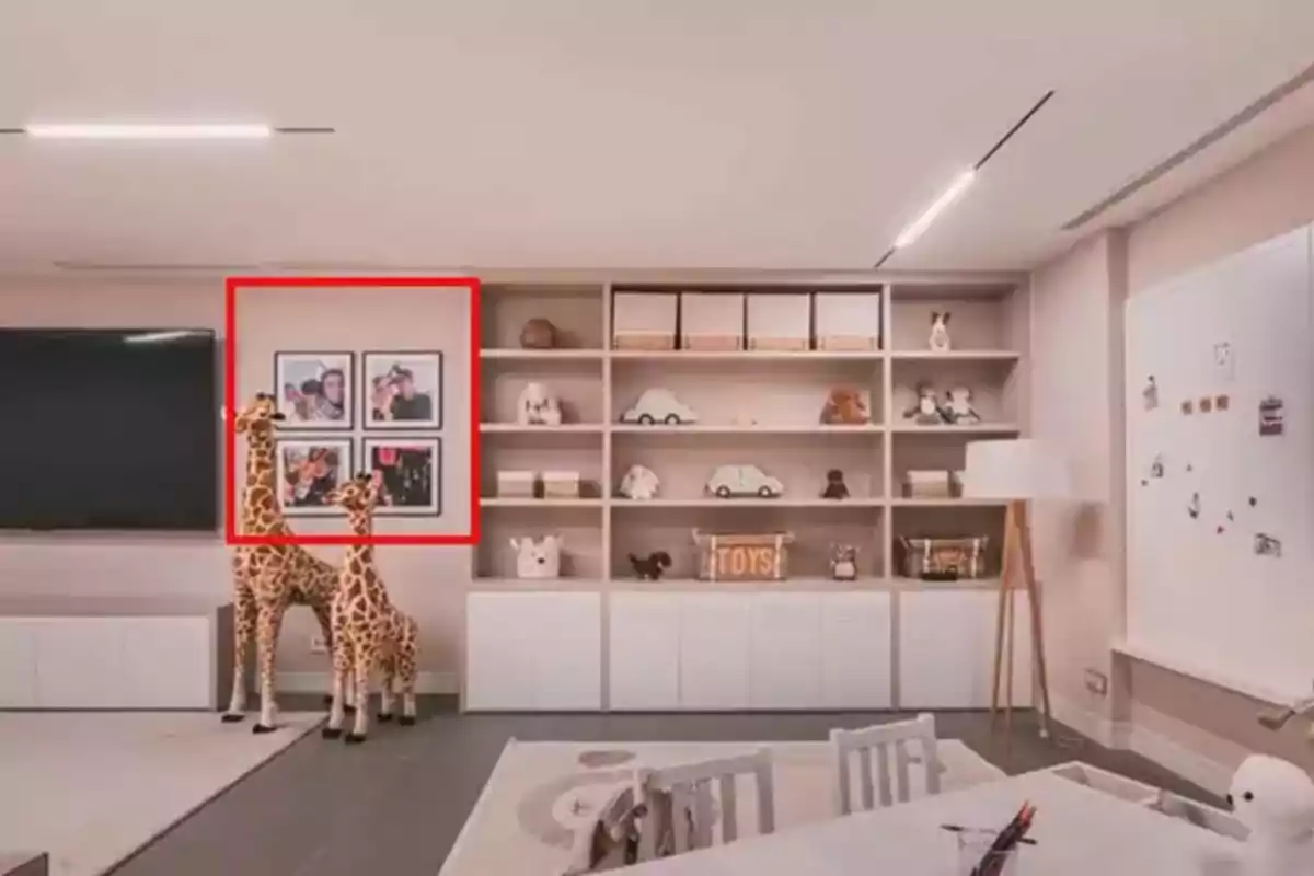 Una sala de juegos infantil con estanterías llenas de juguetes y decoraciones, dos jirafas de peluche grandes, una televisión en la pared y un área de juegos con una mesa y sillas pequeñas. Una sala de juegos infantil con estanterías llenas de juguetes y decoraciones, dos jirafas de peluche grandes, una televisión en la pared y un área de juegos con una mesa y sillas pequeñas.