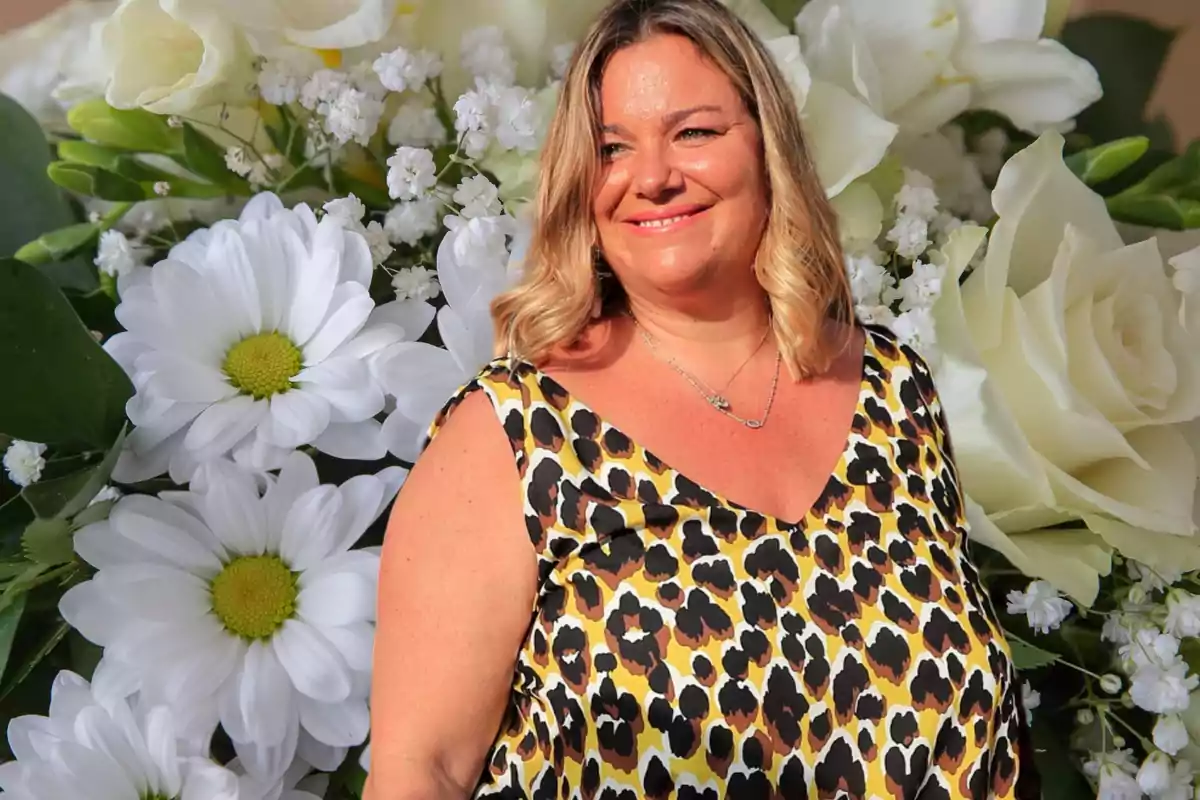 Una mujer sonriente con un vestido de estampado animal frente a un fondo de flores blancas.