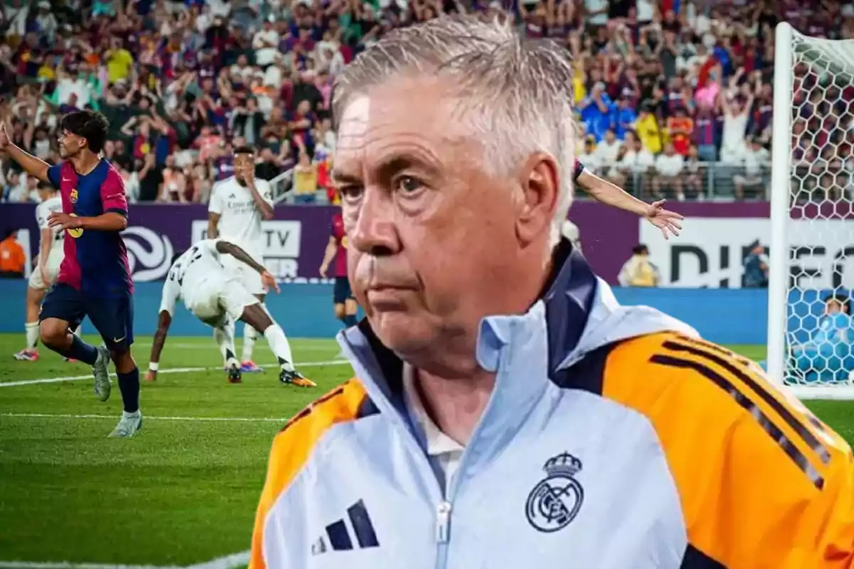 Un entrenador de fútbol con chaqueta del Real Madrid observa el campo mientras un jugador del Barcelona celebra un gol en el fondo.