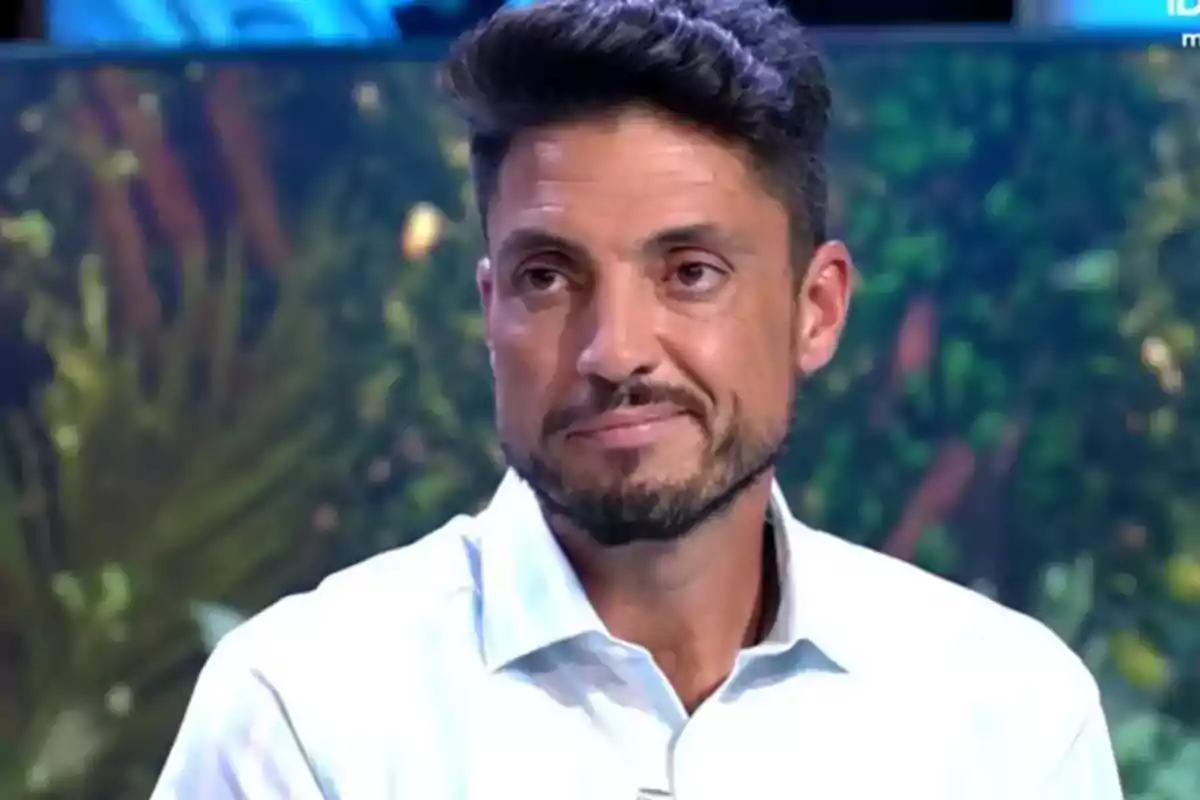 Un hombre con barba y cabello oscuro lleva una camisa blanca y está en un entorno con fondo desenfocado. Un hombre con barba y cabello oscuro lleva una camisa blanca y está en un entorno con fondo desenfocado.
