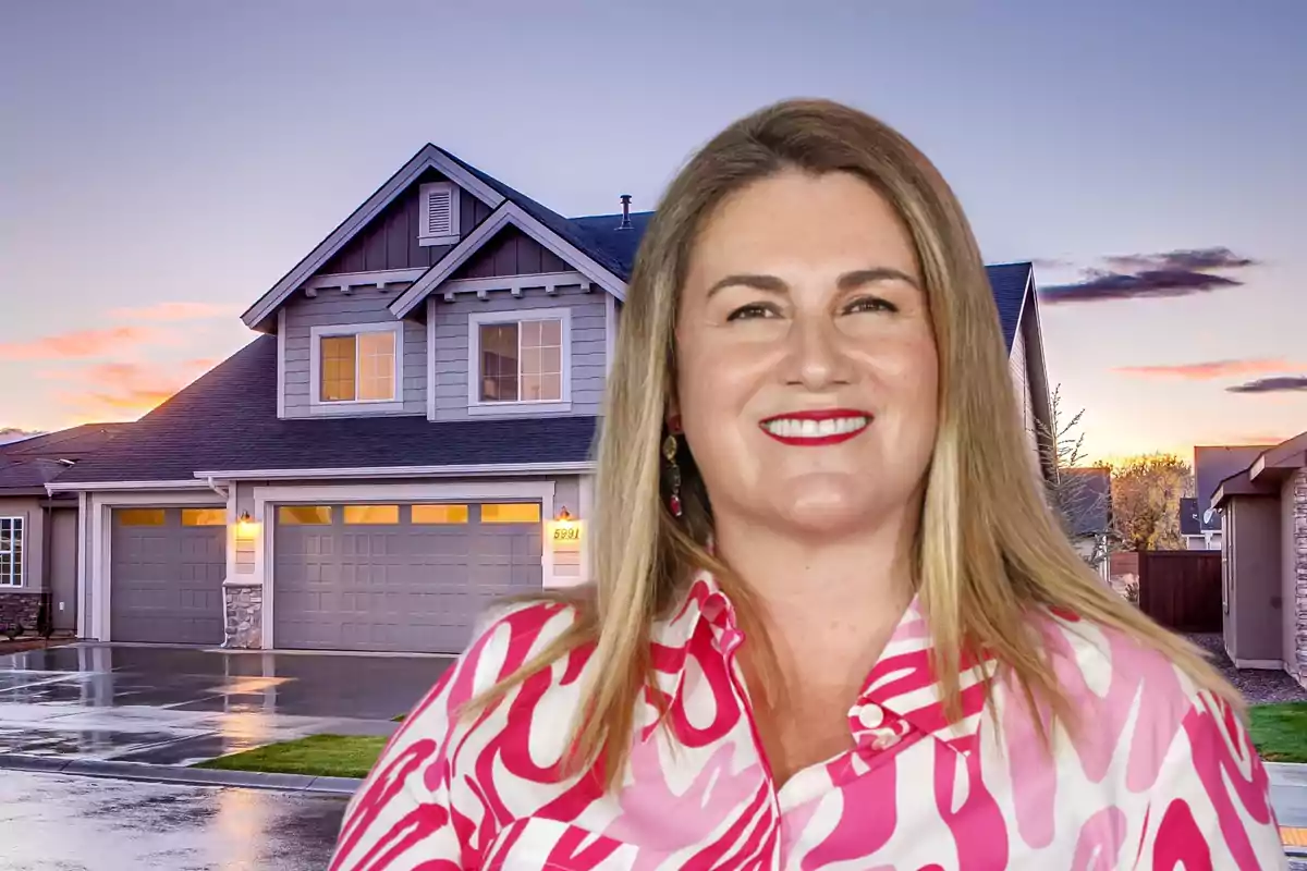 Una mujer sonriente con una camisa de estampado rosa frente a una casa moderna al atardecer.