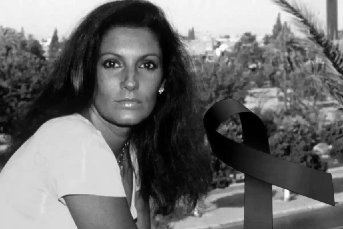 Una mujer de cabello oscuro mira a la cámara en una fotografía en blanco y negro con un lazo negro superpuesto.