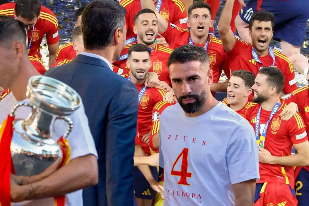 Jugadores de la selección española de fútbol celebran con el trofeo mientras un hombre con una camiseta blanca con el número 4 observa.