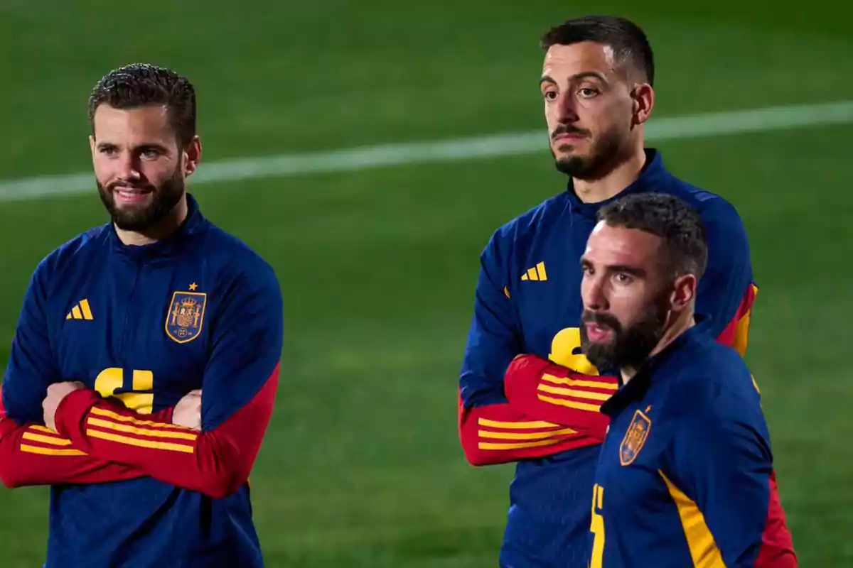 Tres jugadores de fútbol con uniformes de entrenamiento de la selección española están de pie en el campo.