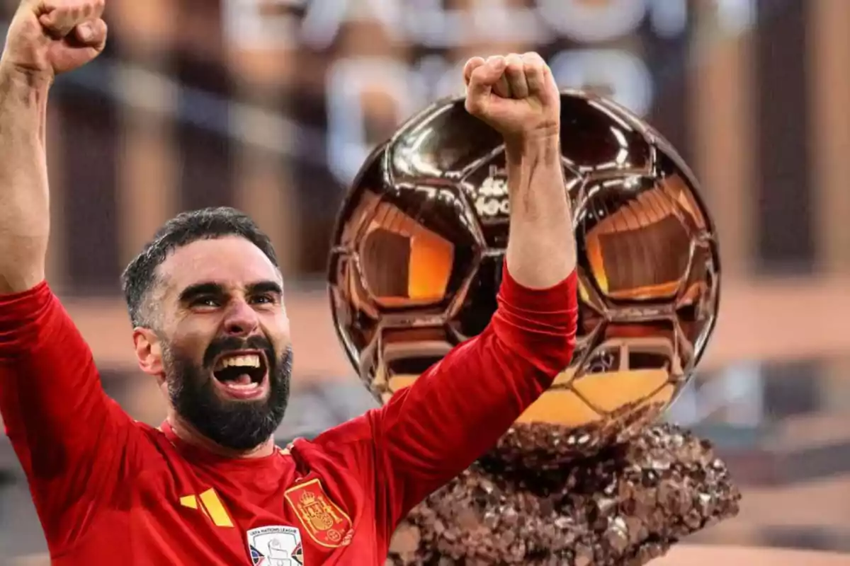 Un jugador de fútbol con uniforme rojo celebra con los brazos en alto frente a un trofeo dorado.