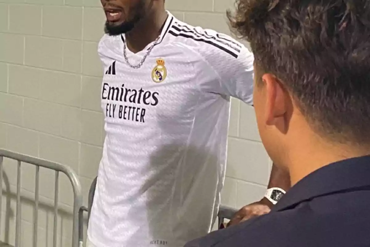 Un jugador de fútbol con la camiseta del Real Madrid hablando con otra persona.