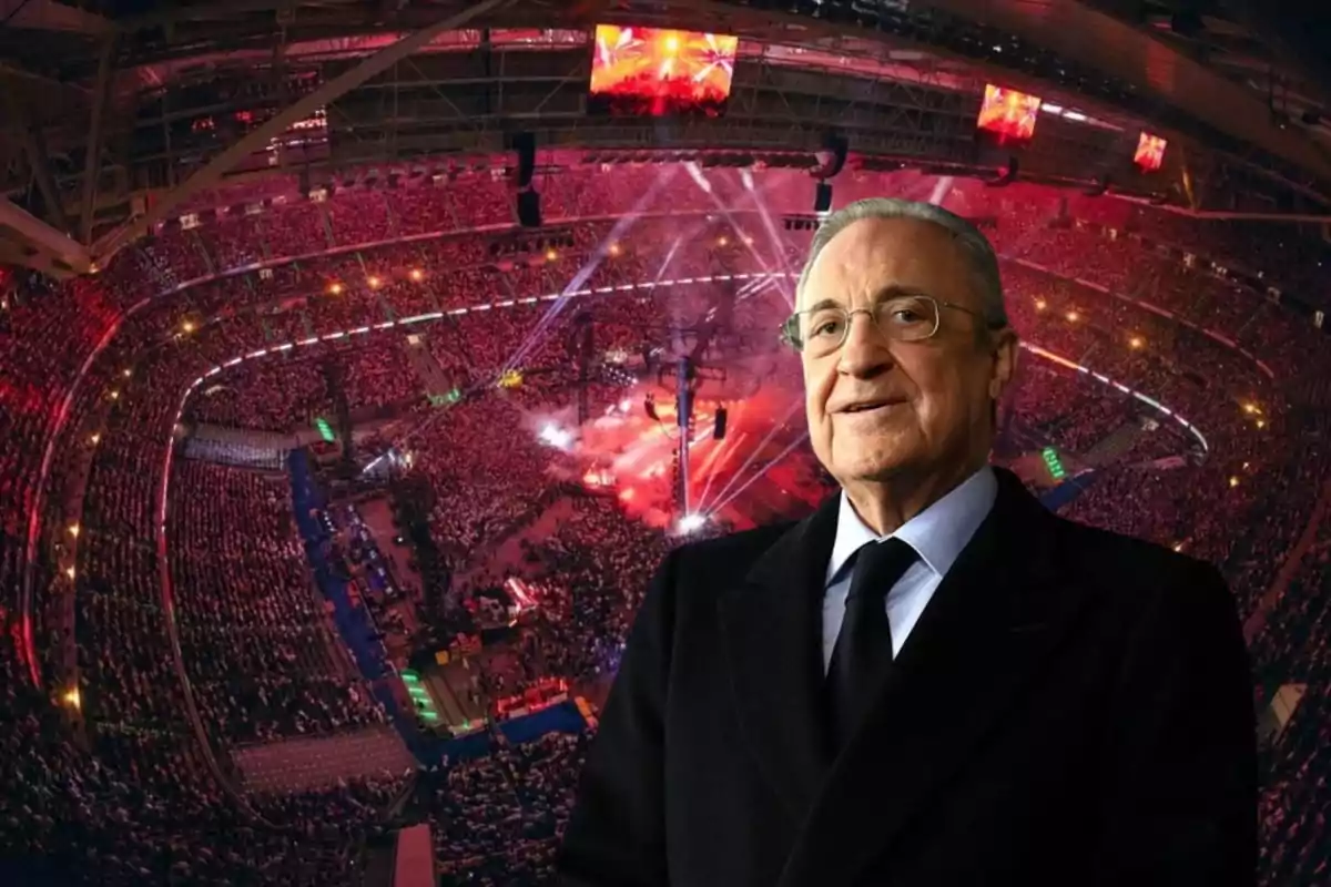 Un hombre mayor con gafas y traje oscuro en primer plano, con un estadio lleno de gente y luces de espectáculo en el fondo.