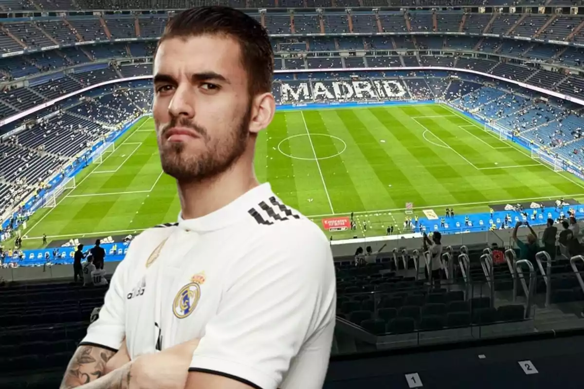 Un jugador de fútbol con la camiseta del Real Madrid está de pie con los brazos cruzados frente a un estadio de fútbol vacío.