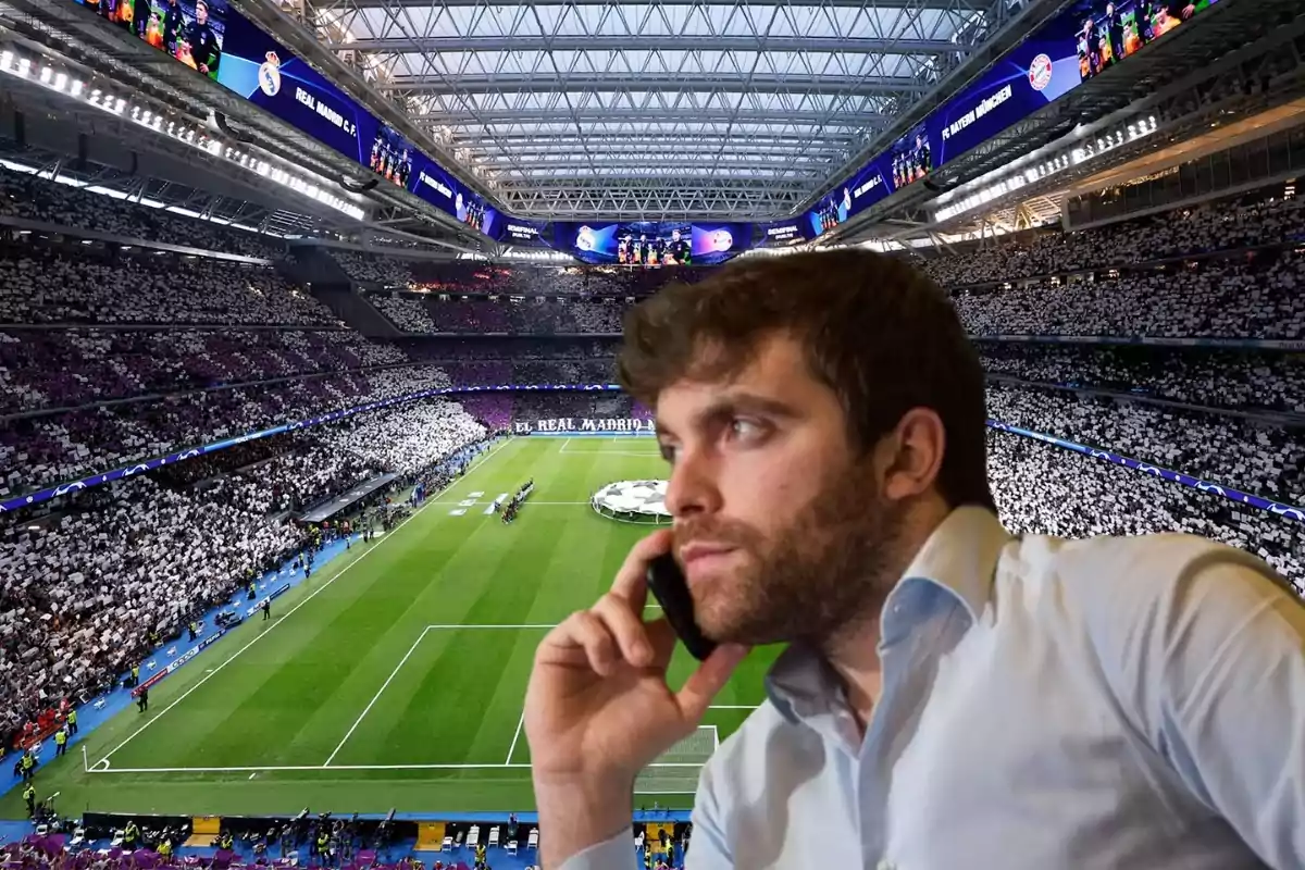 Un hombre hablando por teléfono con un estadio de fútbol lleno de espectadores de fondo.