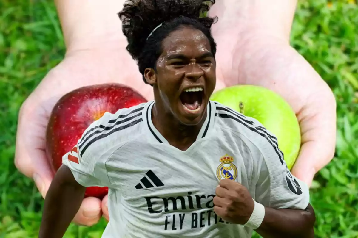 Un jugador de fútbol con uniforme blanco celebra con entusiasmo frente a un fondo de manos sosteniendo una manzana roja y una verde.