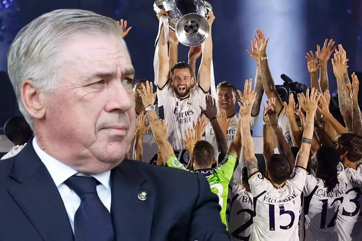 Un hombre de traje en primer plano con un grupo de jugadores de fútbol celebrando con un trofeo en el fondo.