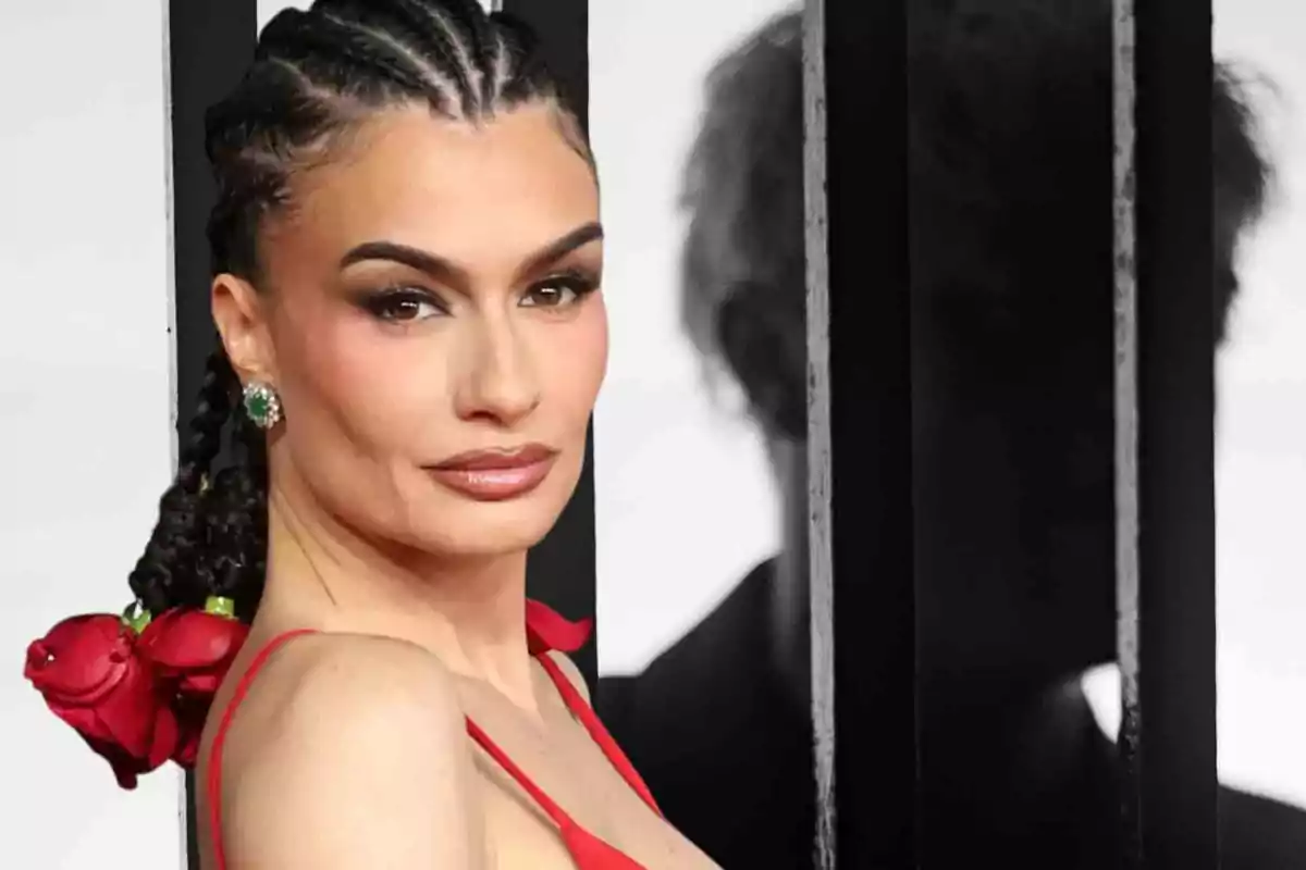 Una persona con trenzas y vestido rojo posa frente a un fondo en blanco y negro.