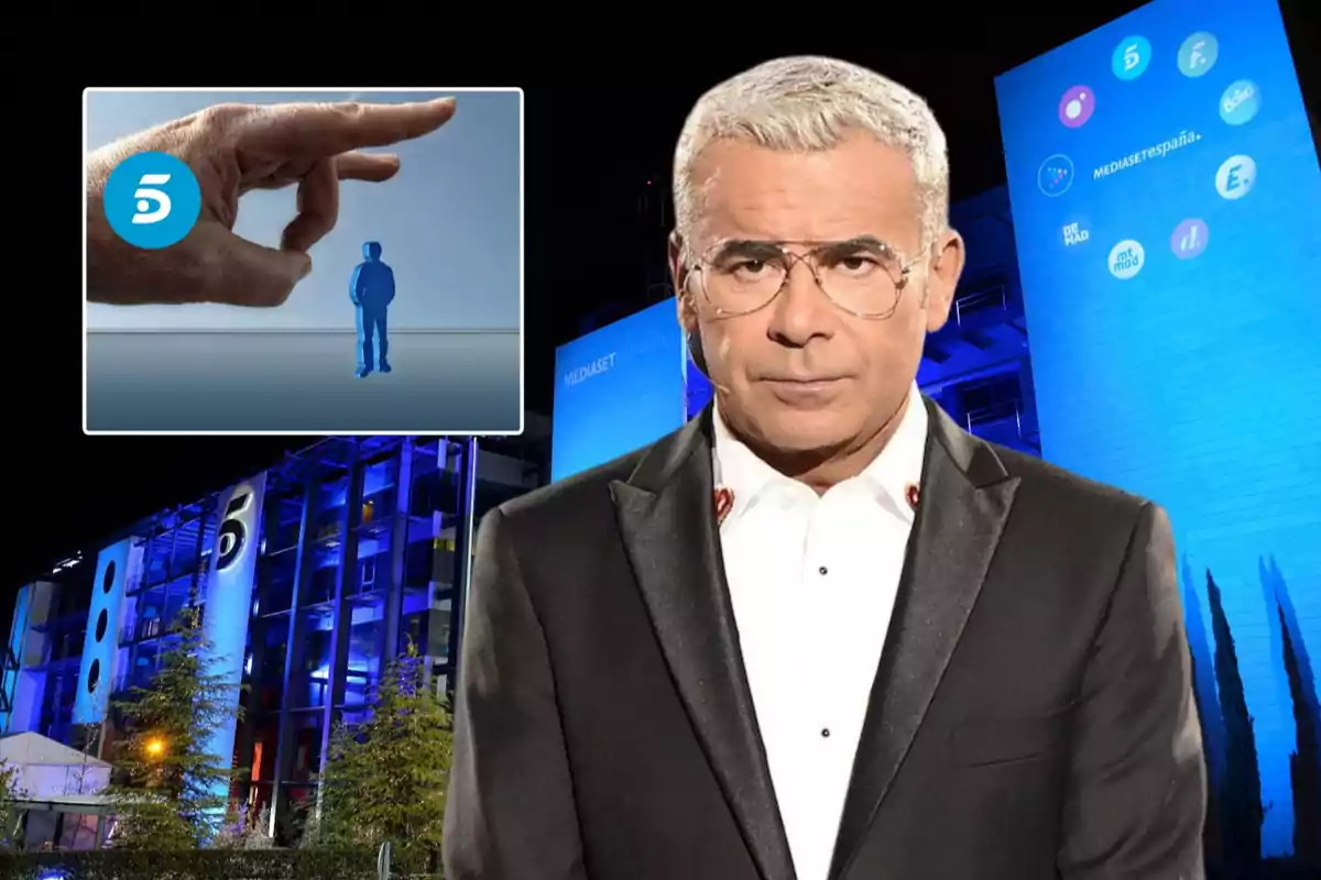 Un hombre con gafas y traje oscuro está frente a un edificio iluminado en azul con logotipos de canales de televisión, mientras en la esquina superior izquierda se muestra una mano gigante apuntando a una figura humana pequeña junto al logotipo de un canal.