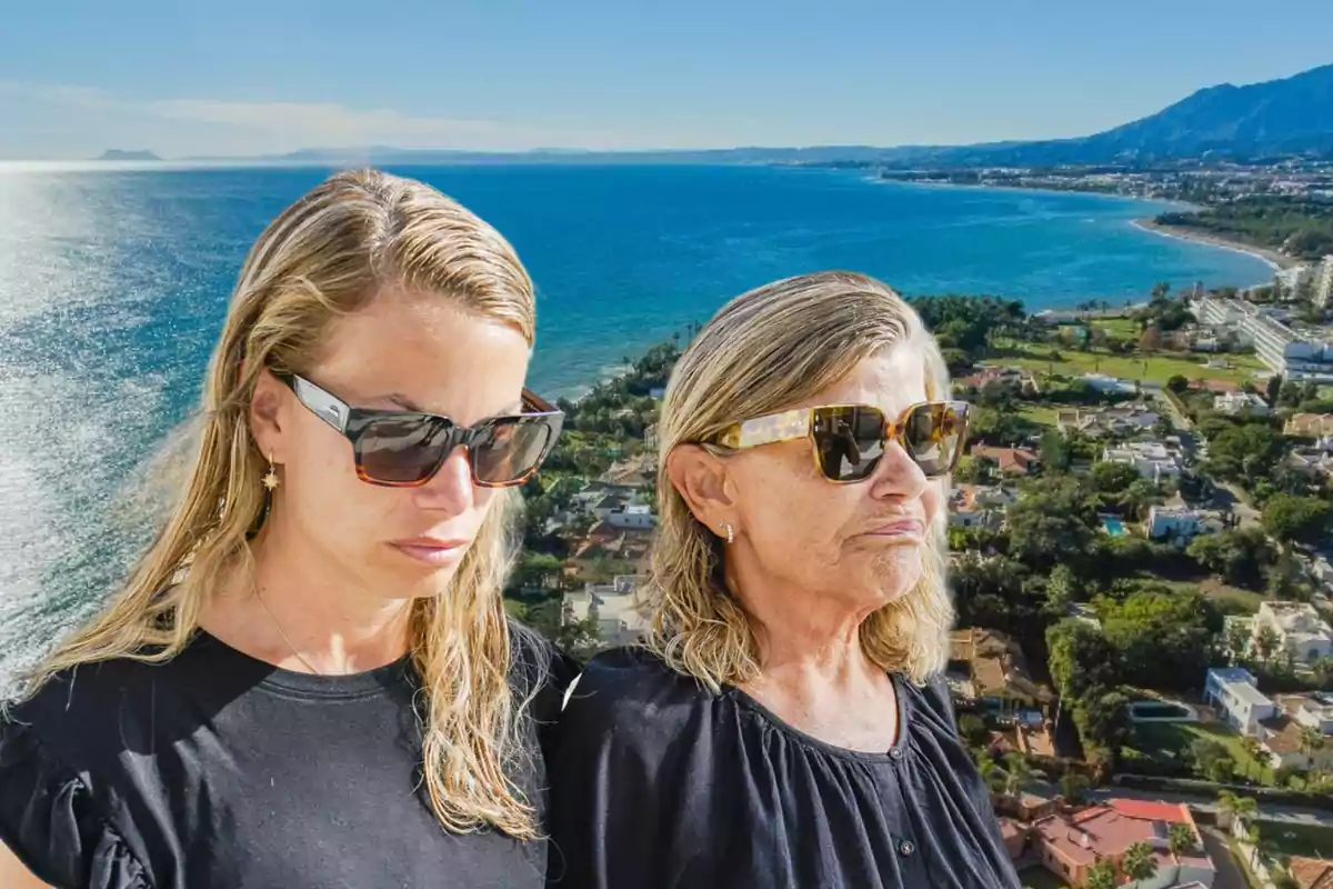 Dos mujeres con gafas de sol posan frente a un paisaje costero con el mar y montañas al fondo.