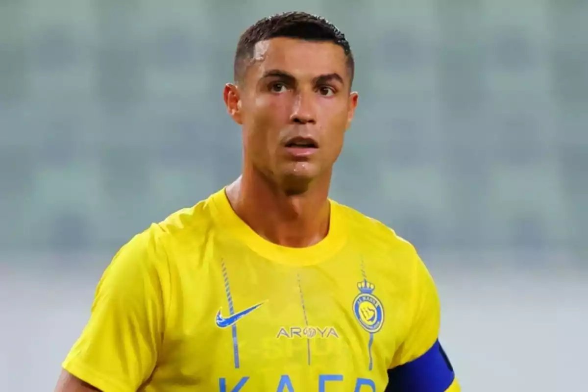 Jugador de fútbol con camiseta amarilla y brazalete azul en el campo.