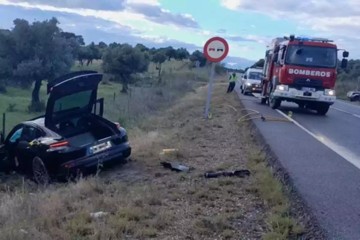 Un coche negro accidentado en la cuneta de una carretera con un camión de bomberos y personal de emergencia en la escena. Un coche negro accidentado en la cuneta de una carretera con un camión de bomberos y personal de emergencia en la escena.