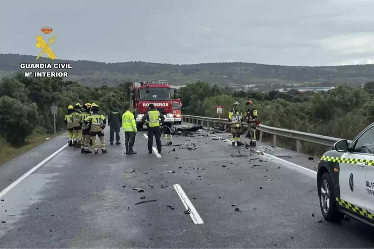 Un grupo de bomberos y personal de la Guardia Civil se encuentra en una carretera atendiendo un accidente con escombros esparcidos por el asfalto y un camión de bomberos presente. Un grupo de bomberos y personal de la Guardia Civil se encuentra en una carretera atendiendo un accidente con escombros esparcidos por el asfalto y un camión de bomberos presente.