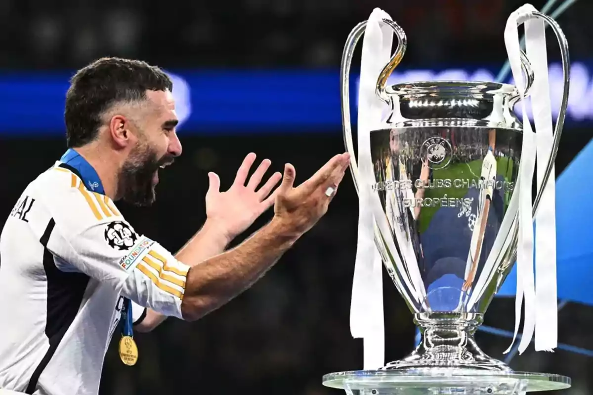 Dani Carvajal con la camiseta del Real Madrid y una medalla al cuello lanzando las manos hacia el trofeo de la Champions League