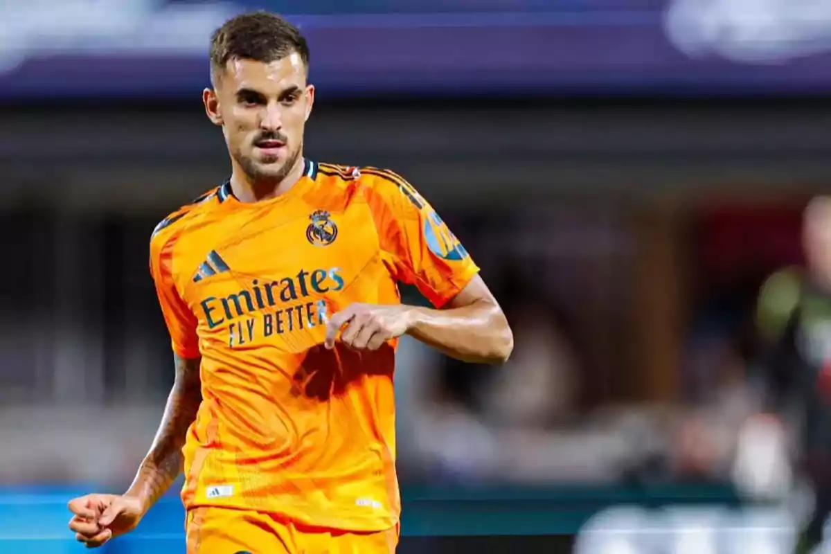 Jugador de fútbol con uniforme naranja del Real Madrid en el campo de juego.